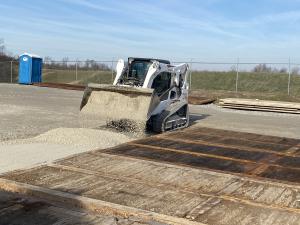 Skid-Steer placing stone around mats to level area